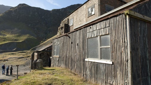 Visitors about to enter Force Crag Mine on a sunny day with the old building in the foreground and Coledale Valley behind